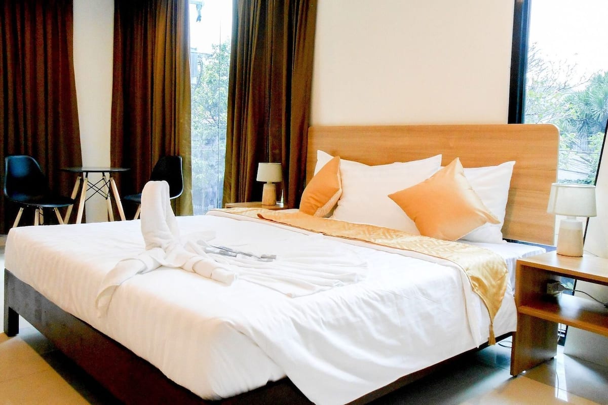 A hotel room with a large bed, two bedside tables, a chair, and a view of greenery outside.