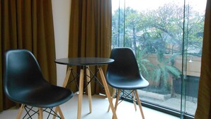 A room with two black chairs and a small round table, a large window with curtains, and a view of trees and buildings outside. - Rublin Hotel (Cebu City)
