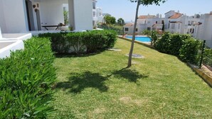 A well-maintained grassy area with a pool, surrounded by white buildings and greenery.