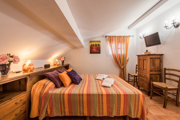 Un dormitorio con cama, cómoda de madera, televisor y un cuadro en la pared.