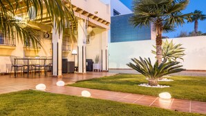 Un bâtiment moderne doté d’un patio comprenant une table et des chaises, le tout entouré d’une pelouse bien entretenue et de palmiers.