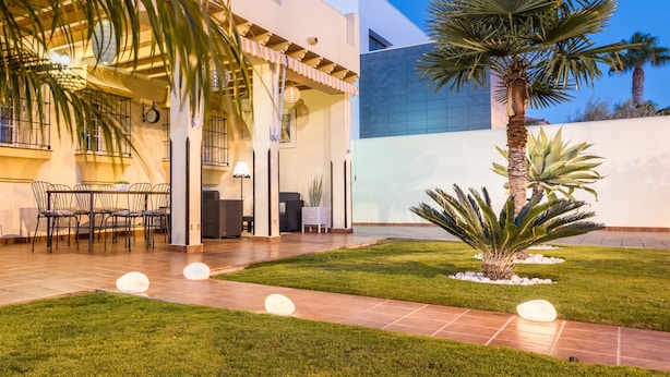 A modern building with a patio area featuring a dining table and chairs, surrounded by well-maintained grass and palm trees.
