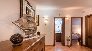A hallway with a wooden dresser, a ship model, and wall sconces.