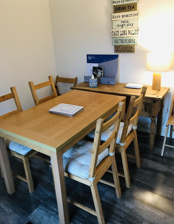 Ett matbord i trä med stolar, en näsduksask, en förpackning näsdukar, en liten bordslampa och en vägg med motiverande citat.
