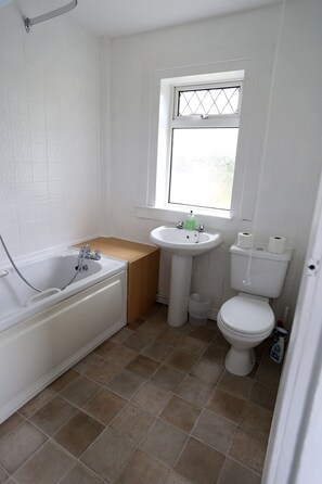 Une petite salle de bain propre, équipée d’une baignoire, d’un lavabo, de toilettes et d’une fenêtre.