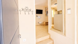 A hallway with a beige wall, a large mirror, a flat-screen TV mounted on the wall, and a wooden bench. - Centrally located apartment for 6,Tarifa (TARIFA)