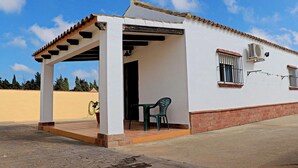 A single-story building with a covered patio area, a window with bars, and a brick base. - Bungalow in complex with shared pool (CONIL DE LA FRONTERA)