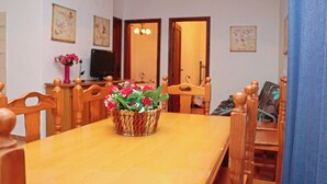 A dining area with a wooden table, chairs, a woven basket with flowers, a television, and a door leading to another room. - Bungalow in complex with shared pool (CONIL DE LA FRONTERA)