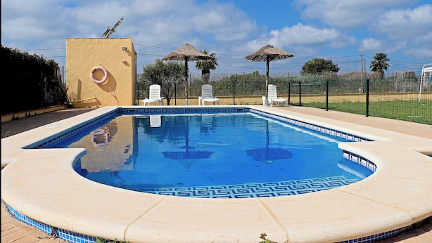 A swimming pool with a tiled edge, surrounded by lounge chairs and a fence. - Bungalow in complex with shared pool (CONIL DE LA FRONTERA)