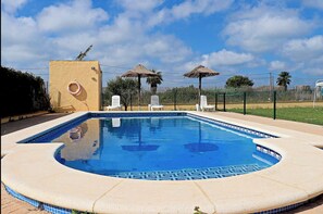 A swimming pool with a tiled edge, surrounded by lounge chairs and a fence. - Bungalow in complex with shared pool (CONIL DE LA FRONTERA)