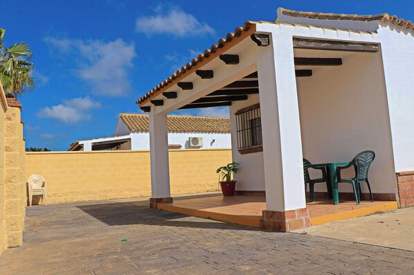 A covered outdoor patio with a table and chairs, a potted plant, and a clear blue sky. - Bungalow on a complex with shared pool (CONIL DE LA FRONTERA)