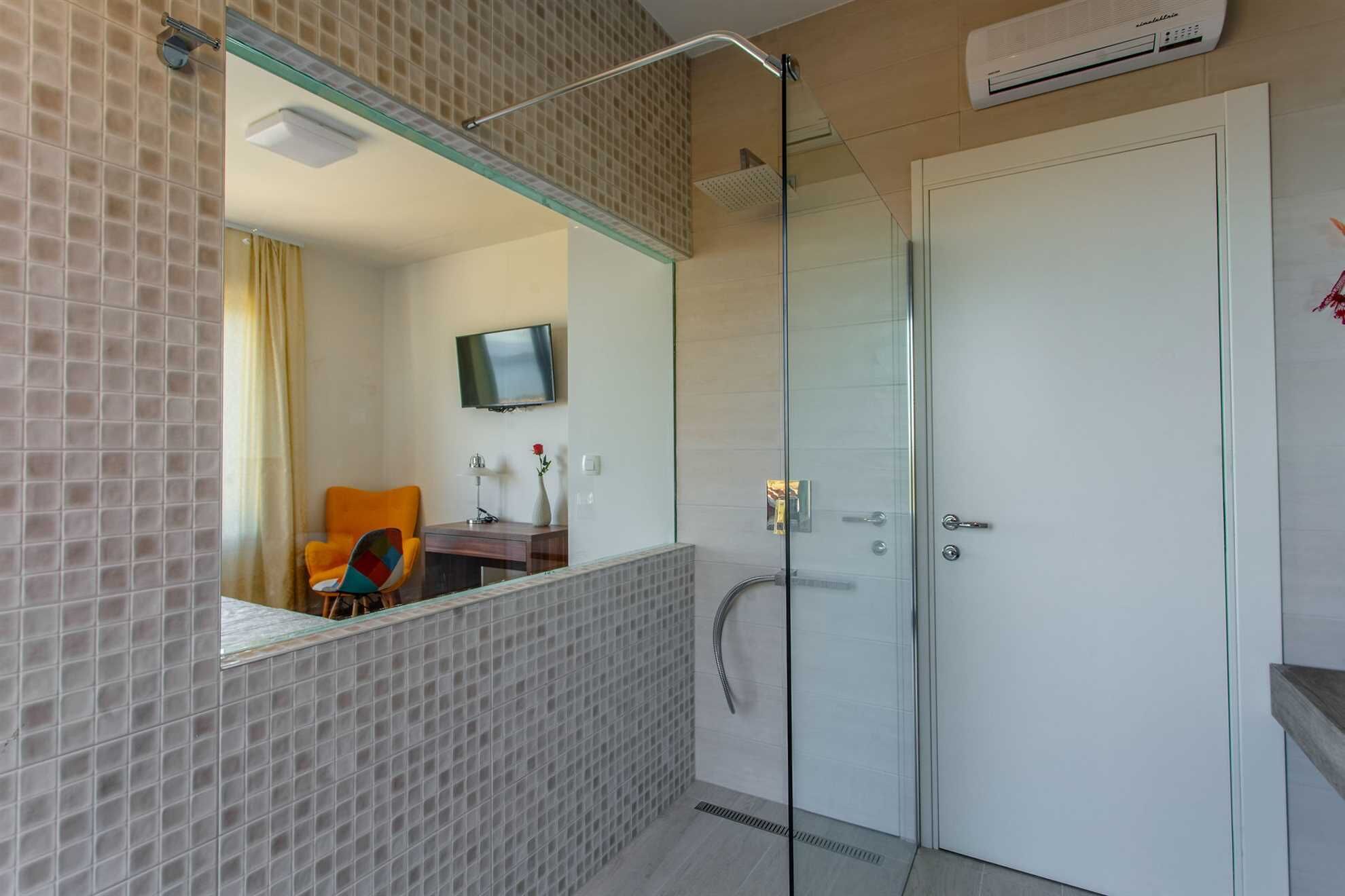 A modern bathroom with a glass shower enclosure, a white door, and a mounted TV.