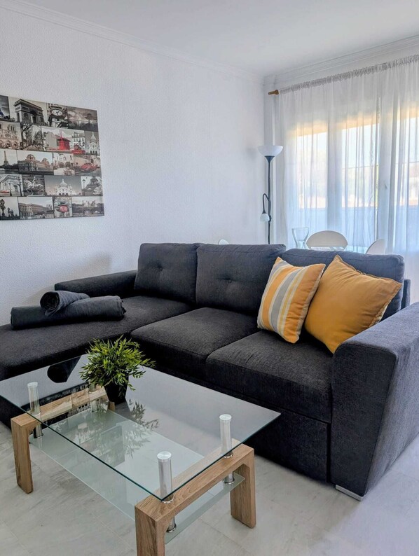 A modern living room with a dark grey sofa, a glass coffee table, and a wall-mounted picture of cityscapes.