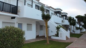 A white building with balconies, a staircase, and a small tree in the foreground.