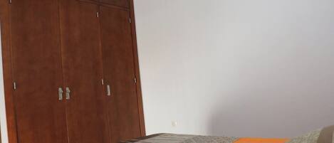Ein Schlafzimmer mit Holzschrank, Teppich mit Muster und orangefarbenem Bettüberwurf.