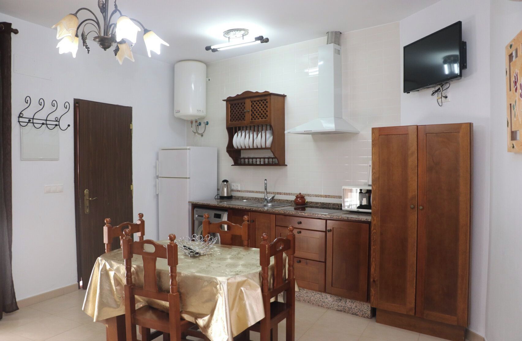 A compact kitchen with a dining table, chairs, a built-in oven, a microwave, and a TV mounted on the wall.