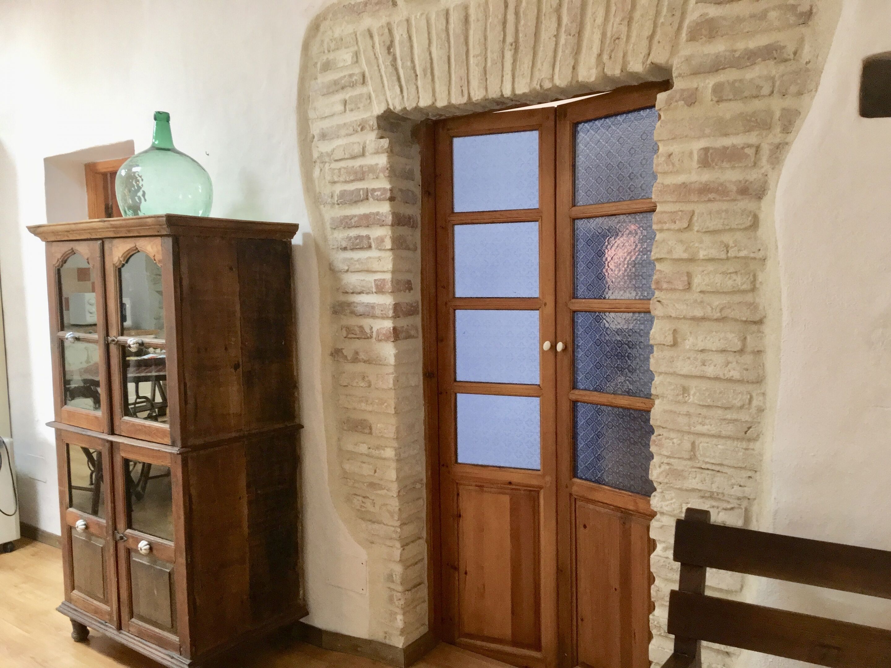 A corner room with a wooden cabinet, a door with frosted glass panels, and a bench.