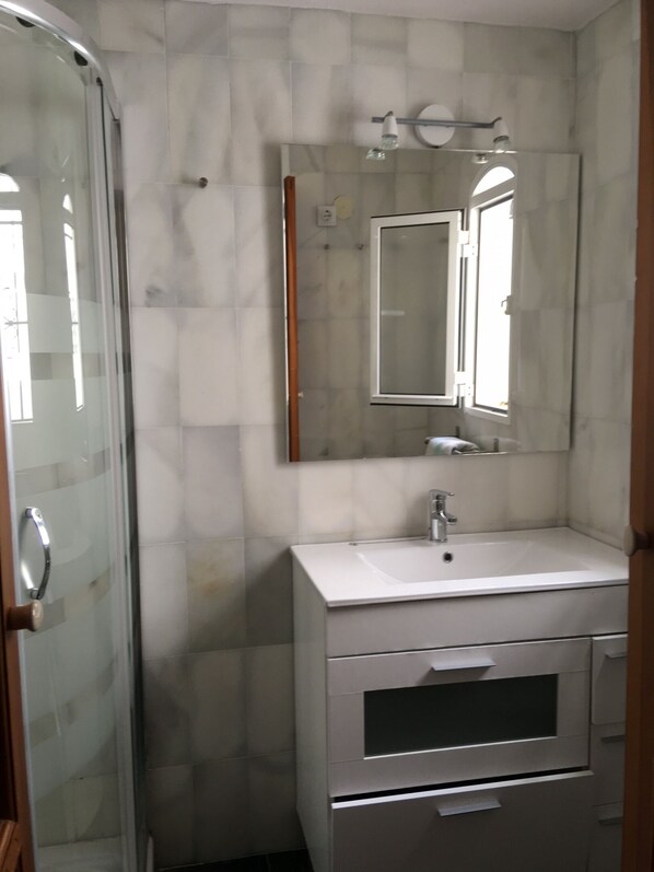 A bathroom with a glass shower enclosure, a white sink, a mirror, and a vanity with drawers. - 3 bedroom house in Tarifa old town (Tarifa)