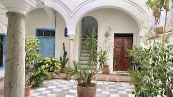 A courtyard with a checkered floor, white columns, and various potted plants.