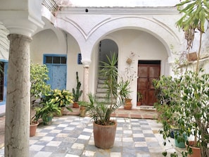 A courtyard with a checkered floor, white columns, and various potted plants. - 3 bedroom house in Tarifa old town (Tarifa)