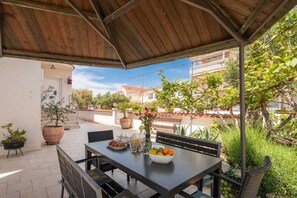 Un espacio al aire libre cubierto con comedor, una mesa para dos, rodeado de plantas en macetas y vistas al vecindario.