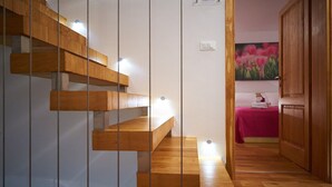 A wooden staircase with built-in lighting, leading to a bedroom with a pink bedspread and a painting of flowers. - Luxury Villa Venera with Pool (Jesenice)