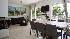 A modern living room with a sofa, a dining table with chairs, a TV, and a painting on the wall. - Luxury Villa Venera with Pool (Jesenice)