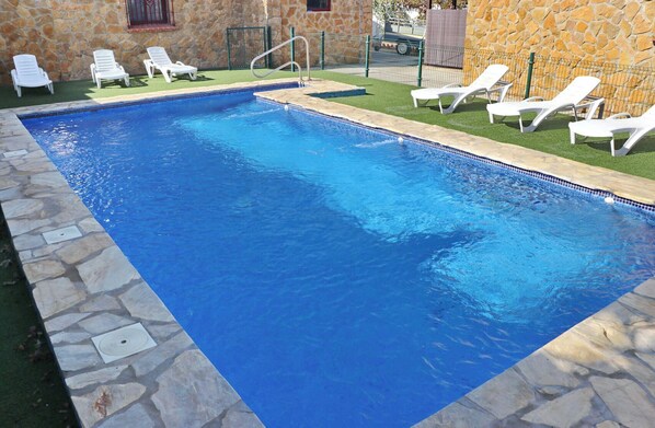 Ein rechteckiger Swimmingpool mit Steinbordierung, umgeben von weißen Liegestühlen und einer Steinmauer.