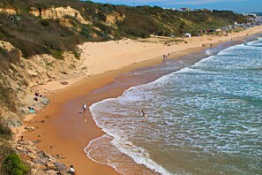 Ein Strand mit badenden Menschen, Sandküste und einem felsigen Felsen.