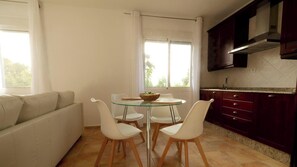 Une cuisine moderne avec des meubles de couleur sombre, une table à manger en verre et un canapé beige.