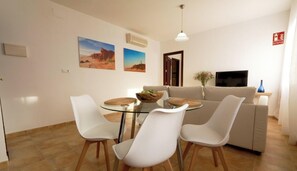Ein Wohnzimmer mit Glastisch, weißen Stühlen, einem beigefarbenen Sofa und zwei Wandbildern mit Wüstenthema.