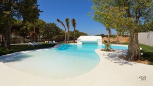 A swimming pool with lounge chairs, surrounded by trees and a white building.