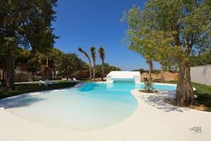 A swimming pool with lounge chairs, surrounded by trees and a white building.