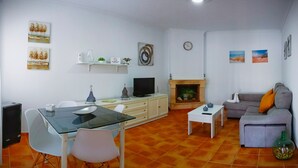 A living room with a glass-top dining table, white chairs, a grey sofa, a white coffee table, a fireplace, and a TV. - Villa Mari Carmen, with pool and BBQ (chiclana de la frontera)