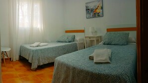 A hotel room with two beds, a small table, a chair, and a painting on the wall. - Villa Mari Carmen, with pool and BBQ (chiclana de la frontera)