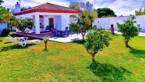 A white house with a red-tiled roof, a patio with chairs, and a small garden with trees. - Villa Mari Carmen, with pool and BBQ (chiclana de la frontera)