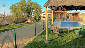 Ein Garten mit Schwimmbecken, einer Pergola und einem eingezäunten Bereich mit Bank und Stuhl.