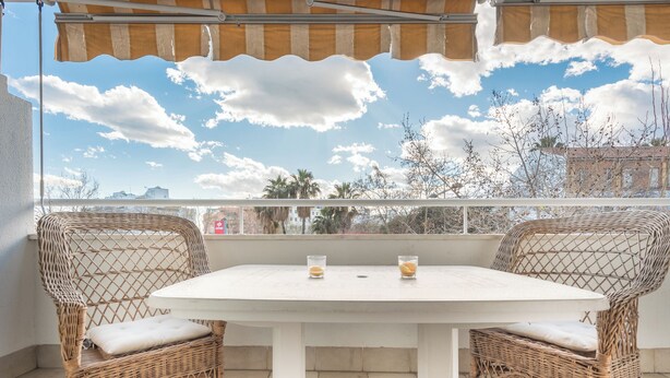 A balcony with wicker chairs and a white table, overlooking a cityscape with buildings and trees. - Apartment with free parking in Marbella (Marbella)