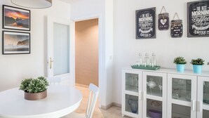 A dining area with a white table, chairs, a potted plant, a cabinet with glass doors, and wall art. - Apartment with free parking in Marbella (Marbella)