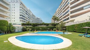 A swimming pool surrounded by a well-maintained lawn, with multiple balconies on adjacent buildings. - Apartment with free parking in Marbella (Marbella)