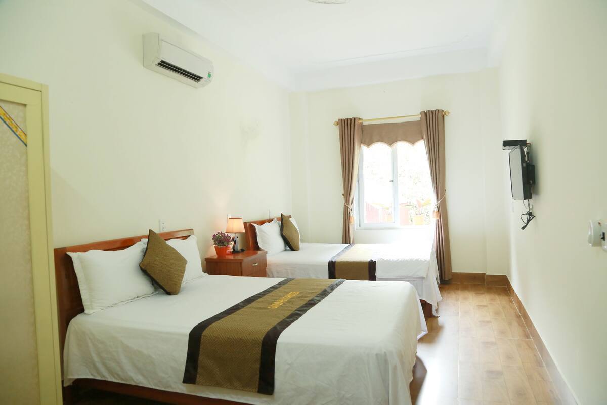 Quarto de hotel com duas camas, ar condicionado, televisão e janela com cortinas.