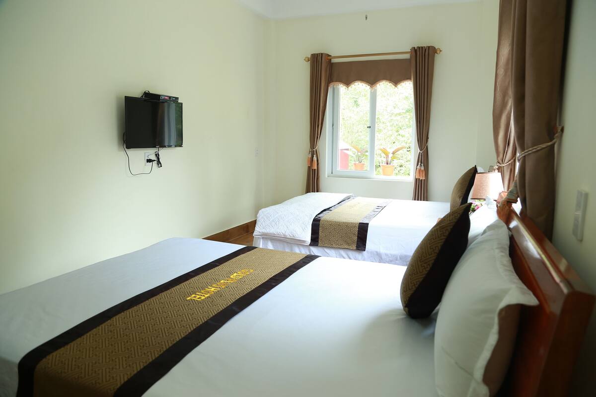 Quarto de hotel com duas camas, uma TV de tela plana na parede e uma janela com cortinas.