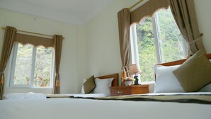 A hotel room with a bed, bedside table, lamp, and curtains. - Gold Plus Hotel (Phong Nha)