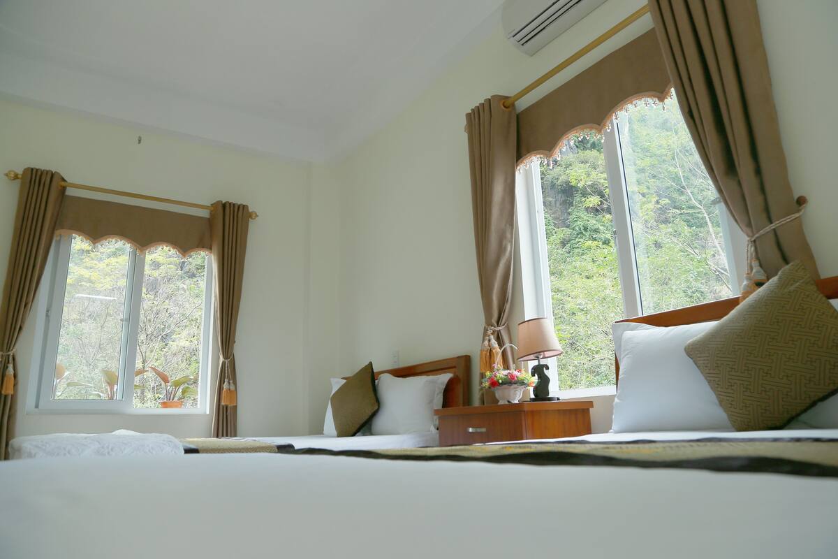 Quarto de hotel com cama, mesa de cabeceira, luminária e cortinas.