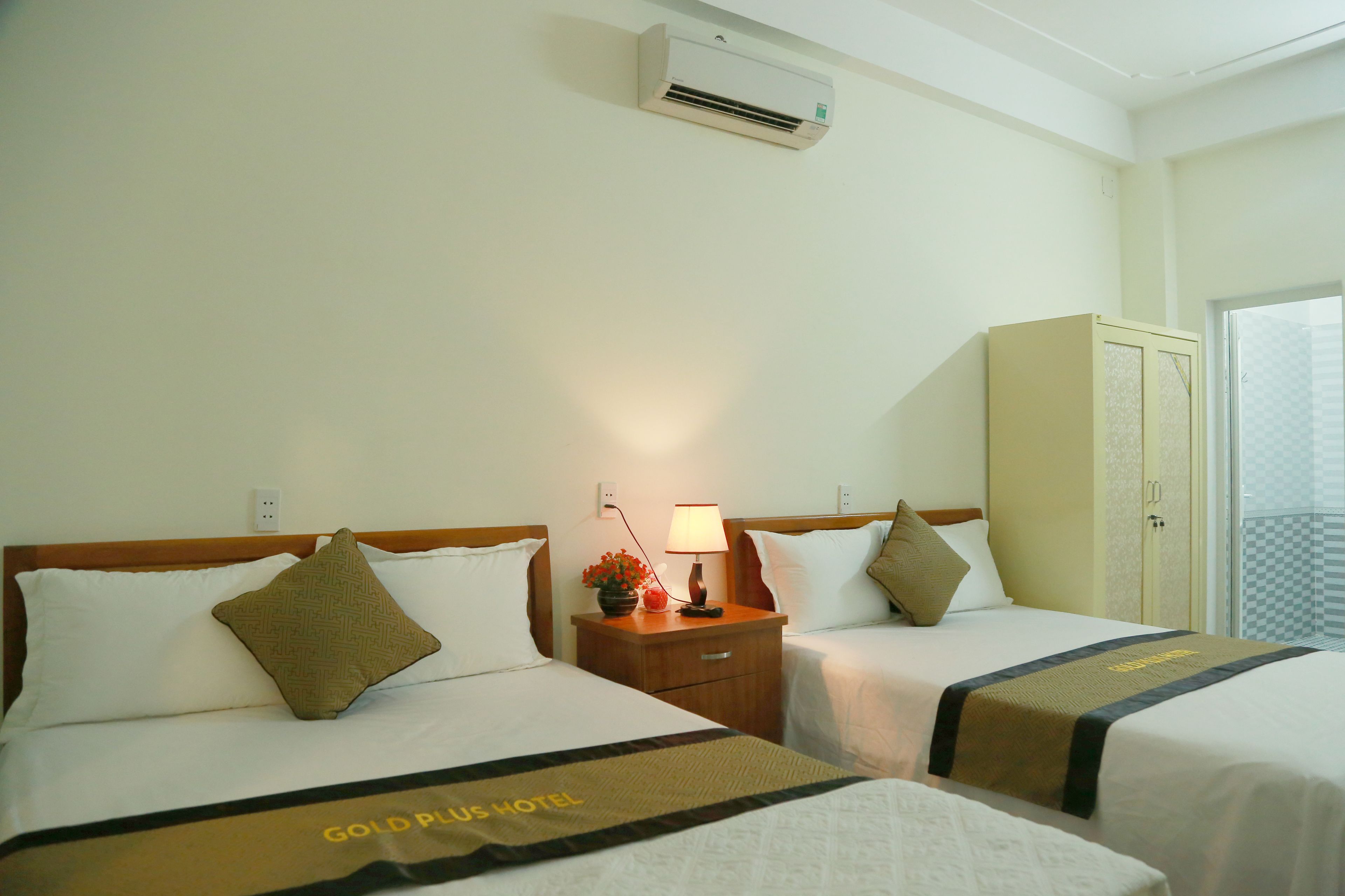A hotel room with two beds, a nightstand with a lamp, an air conditioner, and a wardrobe.