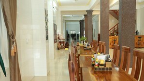 A spacious dining area with a long wooden table and chairs, a buffet setup, and a staircase leading to an upper level. - Gold Plus Hotel (Phong Nha)