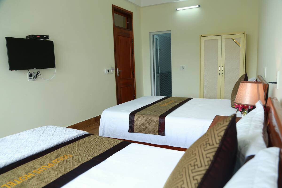 Quarto de hotel com duas camas, uma televisão na parede, uma porta e um abajur.