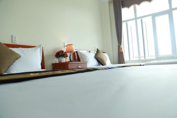 A hotel room with a bed, a nightstand, a lamp, and a window with curtains. - Gold Plus Hotel (Bo Trach)