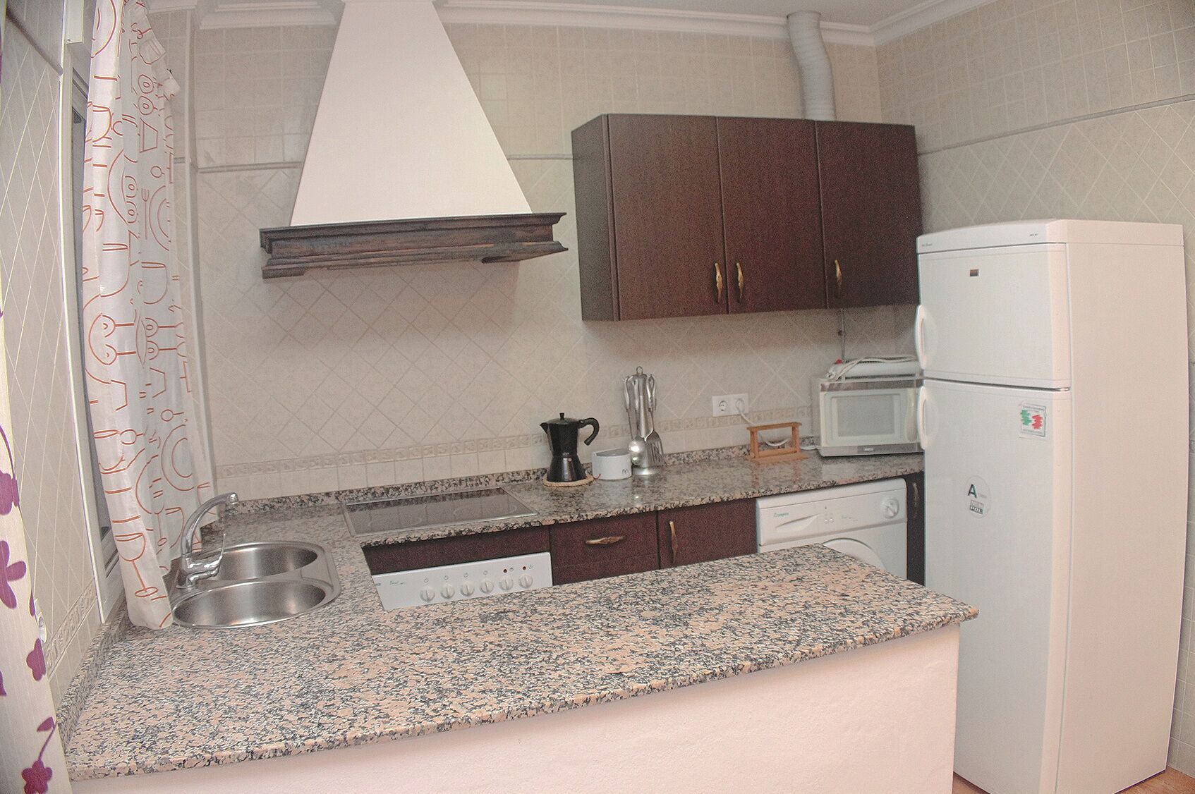 Cocina compacta con encimeras de granito, estufa integrada, microondas, refrigerador y armarios de madera.