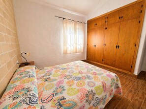 Une chambre à coucher avec un lit, une fenêtre avec des rideaux, une armoire et un mur en briques.